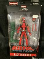 Front view of sealed Marvel Legends Lady Deadpool action figure with swords, alternate heads and hands, and the green Build-A-Figure leg piece visible in packaging.