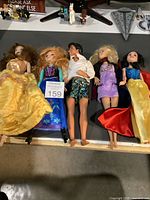 Lot of six dolls including five Disney princess dolls and one male doll laid out on a display surface. Dolls show minor wear, clothing disheveled and hair tangled.