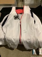 Front view of white Orly jacket showing coral pink zipper lining, black sleeve panels, front pockets and tags attached.
