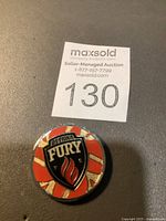 Front view of the round metal commemorative token featuring Ottawa Fury FC logo with red and white striped background and black shield.