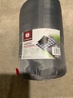 Gray sleeping bag compressed inside the gray stuff sack with the product label showing Outbound branding and information.