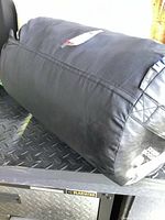 Sleeping bag rolled and packed inside black cylindrical storage bag placed on a metal surface.