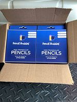 Opened cardboard box showing 2 sealed blue boxes of Pencil Buddies kids triangular pencils.