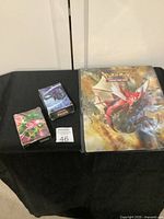 View of Pokemon card album and two deck boxes on black cloth surface displaying artwork and condition.