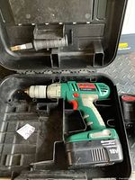 Open black plastic carrying case containing green and black Quantum Pro 18V cordless drill with battery attached. Case has compartments for drill and accessories.