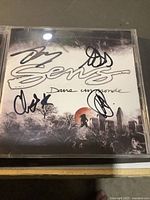 Front cover of 'Dans un monde' CD album by Sens with four signatures on the cover under the jewel case.
