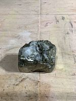 Front view of small natural pyrite mineral specimen showing metallic gold surfaces and white mineral inclusions on a wooden surface.