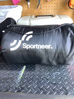 Black Sportneer sleeping bag rolled inside a black carry/storage bag with logo.