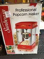 Box of Sunbeam professional popcorn maker front view showing product name, brand, and image of the red popcorn maker with metal kettle and clear panels.
