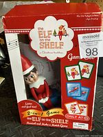 Front view photo of the boxed Elf on the Shelf 2-in-1 Game Set showing elf figure and card illustrations