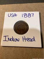 Front side of the coin inside a white cardboard holder labeled USA 1887 Indian Head showing the date and part of the Indian Head design.