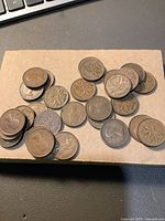 Photo showing over 20 vintage Canadian one-cent coins on a beige surface. Both the obverse and reverse sides of the coins are visible, some showing the maple leaf design and others showing the portrait of Queen Elizabeth II.