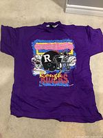 Front full view of purple T-shirt laid flat on floor showing full graphic design of Ottawa Rough Riders helmet and colorful text.