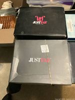 Photo of Just Fab shoe boxes showing two black boxes with the Just Fab logo and one damaged box with sticker and rubber band.