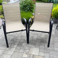 Two beige textilene fabric patio chairs with black metal frames side by side on outdoor tiled floor