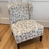 Front view of the beige and white swirl patterned accent chair showing the cushioned seat and backrest with wooden legs.