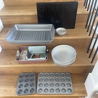 Wide view of all items including baking pans, small molds and placemat on wooden stairs