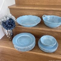 Blue serving dishes arranged on wooden stairs showing 8 dinner plates, 4 smaller plates, and 2 bowls with blue dried flowers in a silver vase.