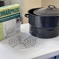 Box for Bernardin Cook's Helper canning rack system next to metal rack and large speckled canning pot with lid on table.