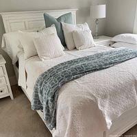 Angle view of bed made with white quilt cover, blue patterned throw draped over edge, and five pillows arranged