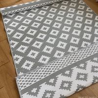 Photo showing the mat partially rolled with its gray and white geometric design and textured weave visible.