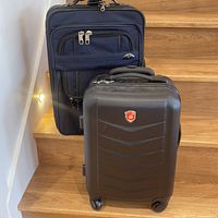 Photo showing two luggage bags, one larger black soft fabric with external zippers, and one medium black hard shell spinner with Canada maple leaf emblem.