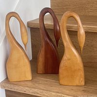 Front view of the 3 Mel Watson hand-carved wooden swan sculptures showing varied wood tones and smooth, curved neck shapes.