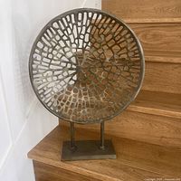 Front view of the abstract metal sculpture featuring a circular open lattice pattern with irregular shaped cutouts, showing overall dimensions and structure.