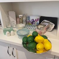 Overview of the lot items including bowl with fruit, salt and pepper shakers, bath products, cutlery set, candle, glass tumbler, and bowls.