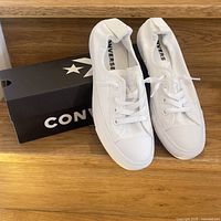 Pair of new white Converse runners with box on wooden surface, showing side and top view