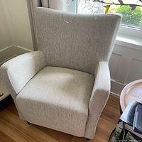 Front view of the beige upholstered occasional chair showing the curved backrest and padded armrests.