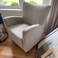 Beige textured upholstered occasional chair angled to show right armrest and backrest near window.