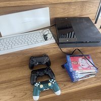 Overview of PS4 console, Apple keyboard, three controllers and stack of game cases