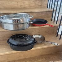 Full set of roasting pans and skillets displayed on wooden stairs, showing size and condition.