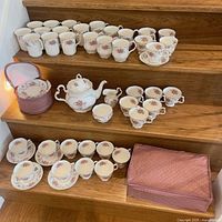 Entire set displayed on wooden stairs: mugs, teapot, sugar bowl, creamer, tea cups with saucers, storage cases.