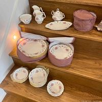 Overview of lot on wooden stairs showing sugar bowls, creamer, platter, plate cases, spare plates and bowls