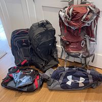 Five sporting bags arranged on floor including backpacks and duffel bags.