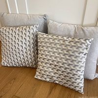 Four Urban Barn accent pillows: two large solid light grey pillows, two smaller pillows with a grey and cream geometric pattern.