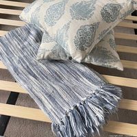 Photo showing two Paisley floral print pillows stacked on a slatted wood surface with blue and white striped fringed throw blanket.
