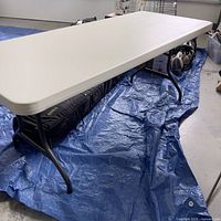 Full view of the white folding table on blue tarp showing its size and leg structure