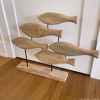 Front view of the wooden fish sculpture showing all five fish attached to metal rods and wooden base.