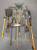 Photo showing 12 assorted gardening tools arranged on the floor against a gray background