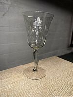 Single vintage crystal wine glass displaying floral etching and faceted stem on light wooden surface.