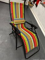 Photo of one folding beach lounger with adjustable back, multicolored striped fabric, and matching neck pillow on black metal frame.