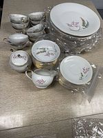 Multiple stacked dinner plates, salad bowls, and soup bowls with floral designs and gold trim, plus teacups with saucers, sugar and milk set, gravy boat, all arranged on a table.