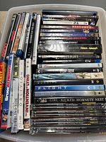 Photo showing a plastic container filled with multiple DVD cases including titles like The Party, The Blind Side, The Invention of Lying, Star Trek, Dunkirk, Flight, Girl Kicked Hornet's Nest, and TV show complete series seasons.