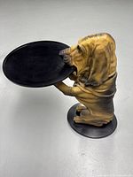Angled view showing brown dog figure holding a round black tray