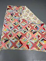 Shows the full quilt front with colorful patchwork and floral backing partially folded to reveal reverse side