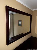 Large rectangular mirror with dark rich wood frame hung on a wall, showing clear reflection and classic design.