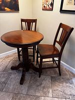 Photo of round maple table with two wooden chairs in a corner of room on tile floor.